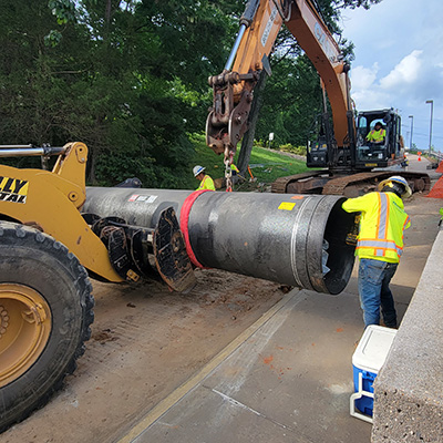 Three construction workers prepare a water main for installation.